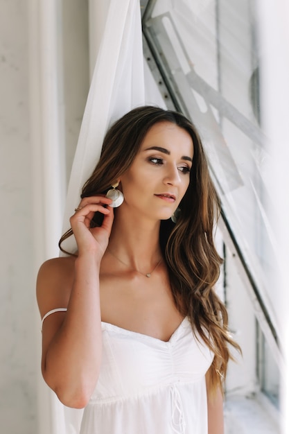 Portrait of a young beautiful sexy woman. Boudoir.  Beautiful girl with long dark hair dressed in white dress