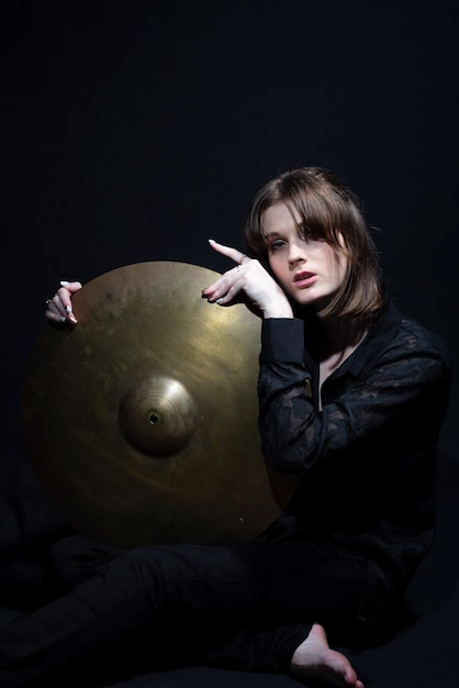 Portrait of young beautiful smiling drummer girl holding drum big cymbal on black background