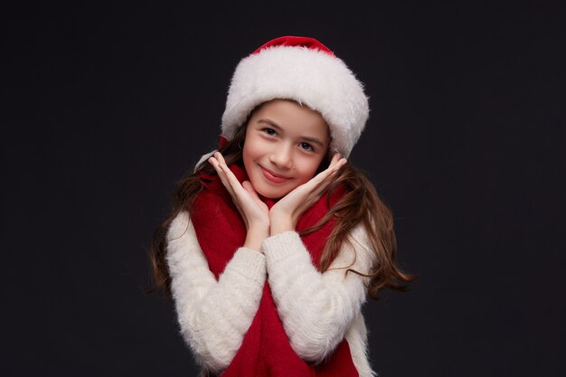 Portrait of young beautiful smiling girl in red Santa hat on a dark background