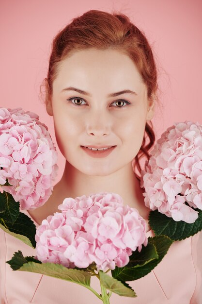 Photo portrait of young beautiful smiling red haired woman with beautiful pinnk flowers around