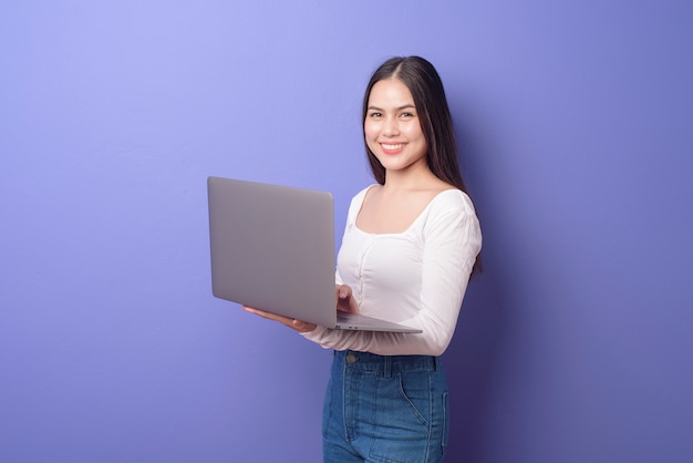 Portrait of young beautiful smiling woman is holding laptop over isolated purple 