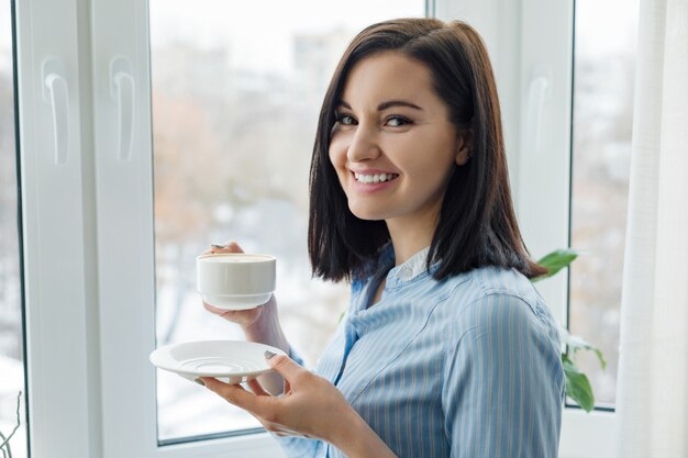 一杯のコーヒーと若い美しい笑顔の女性の肖像画