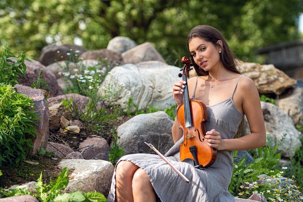 Portrait of a young beautiful violinist on a pile of boulders\
near an old country house