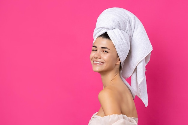 Portrait of young beautiful woman after bath Beauty face of a cheerful attractive girl with towel on head against a pink background