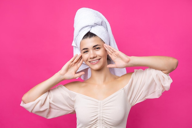 Portrait of young beautiful woman after bath Beauty face of a cheerful attractive girl with towel on head against a pink background