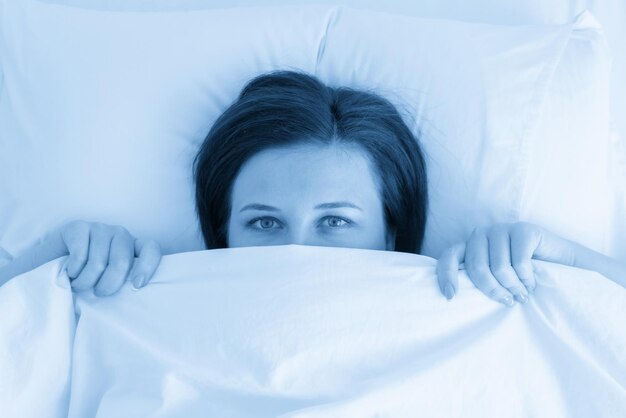 Photo portrait of young beautiful woman in bed looking from under blanket