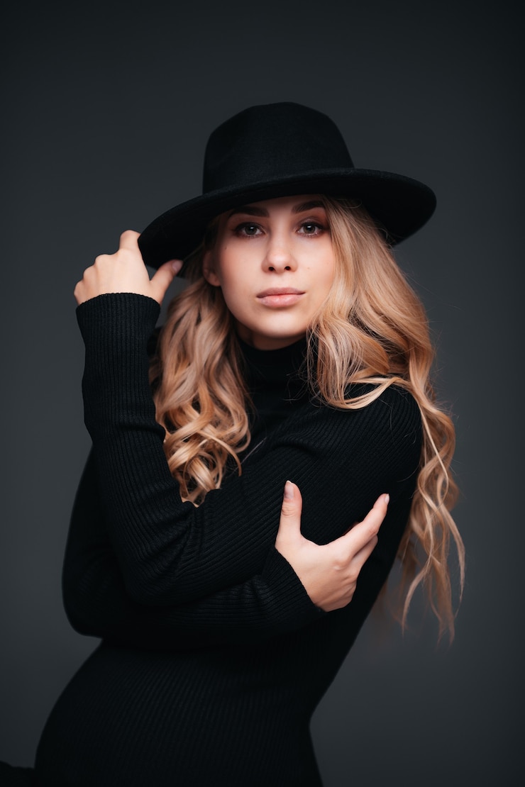 Photo portrait of a young beautiful woman in black hat on black wall