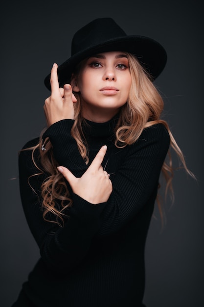 Portrait of a young beautiful woman in black hat on black wall