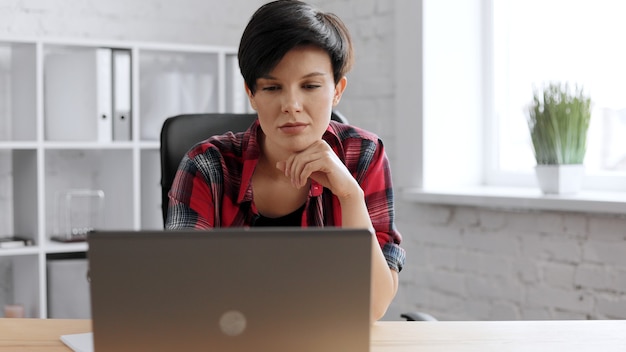 Portrait of young beautiful woman in casual wear with laptop in creative loft office.