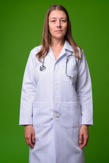 Portrait of young beautiful woman doctor against green wall