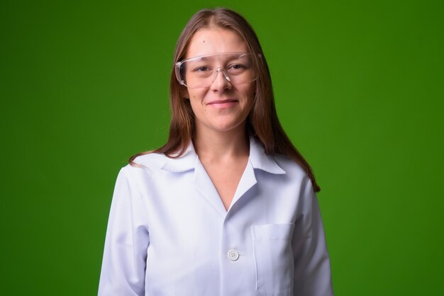 Portrait of young beautiful woman doctor against green wall