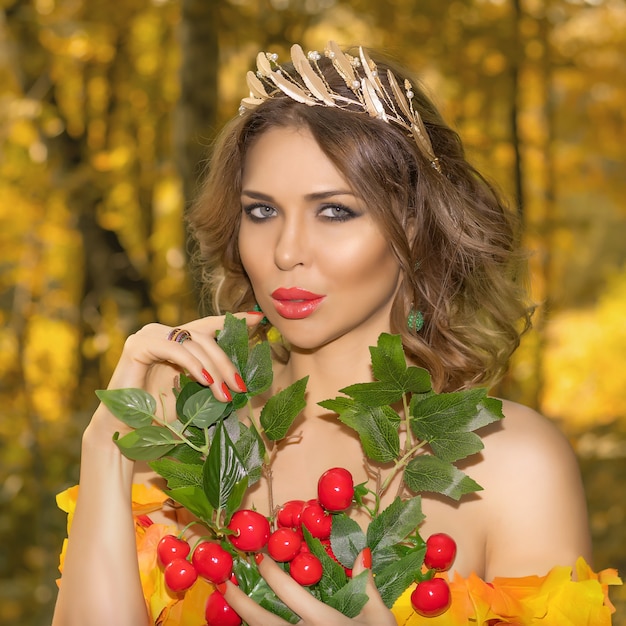 Portrait of a young beautiful woman in a dress made of autumn leaves in the park in autumn season