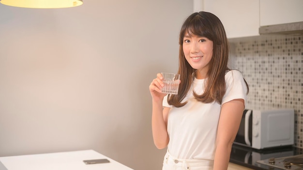 A portrait of young beautiful woman drinking glass of water in kitchen