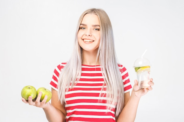 Portrait of young beautiful woman holding in hands glass of water and fresh green apple isolated over white.