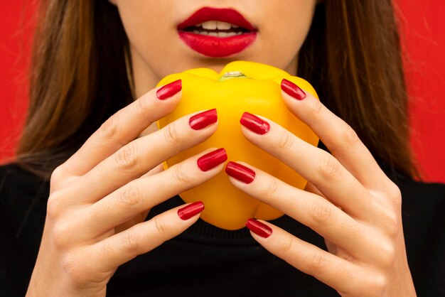 Foto ritratto di una giovane donna bellissima che tiene un pepe giallo su uno sfondo rosso