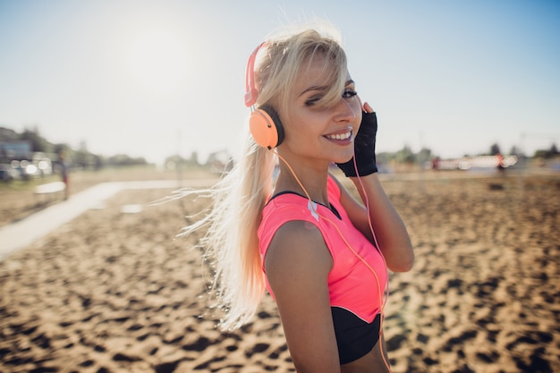 Portrait of young beautiful woman listening to music at beach. Close up face of smiling blonde woman with headphones