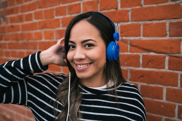 Portrait of young beautiful woman listening to music with blue headphones in the street.