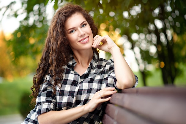 Portrait of young beautiful woman in a plaid shirt and curly hair in summer in the park