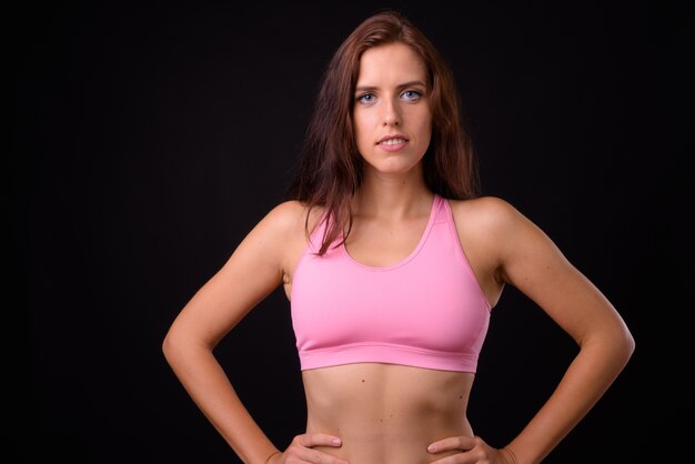 Portrait of young beautiful woman ready for gym against black wall