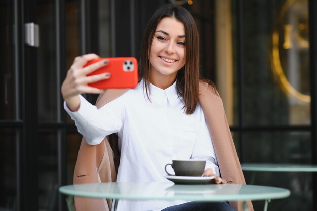 Ritratto di giovane bella donna seduta in un bar all'aperto a bere caffè