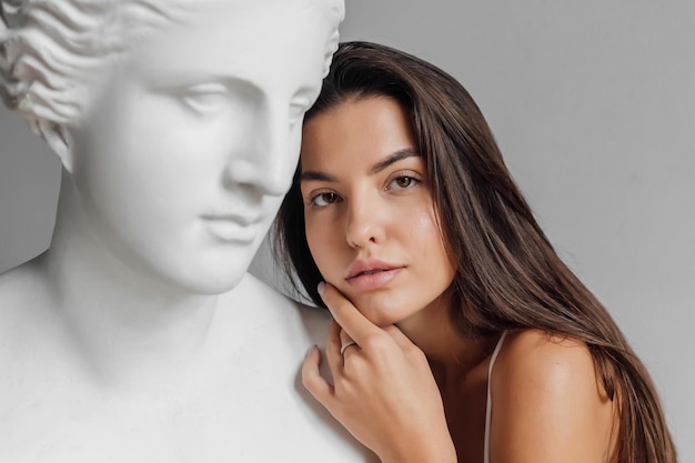 Portrait of young beautiful woman standing near gypsum sculpture venus face