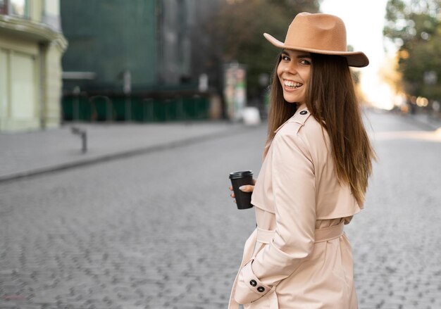 Portrait of a young beautiful woman standing on the street smiling and drinking hot coffee with disposable tableware