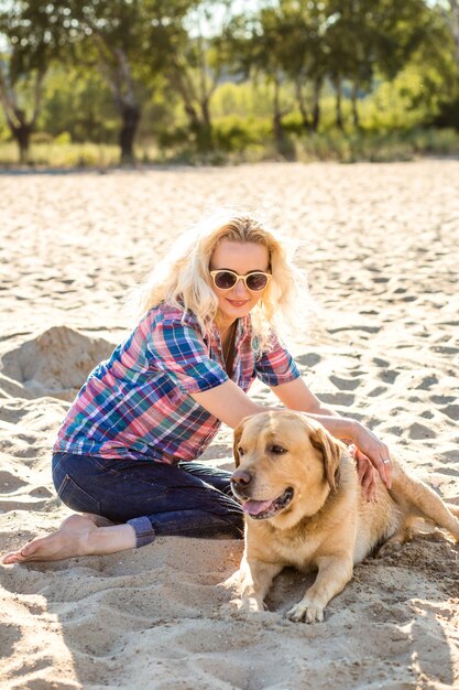 ゴールデンレトリバー犬の女の子と砂浜に座っているサングラスの若い美しい女性の肖像画...