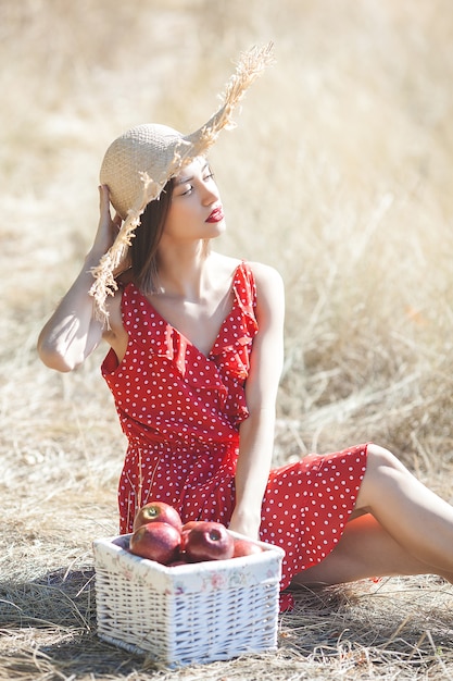 Portrait of young beautiful woman wearing straw hat in summer. Female with fresh apples on the nature.