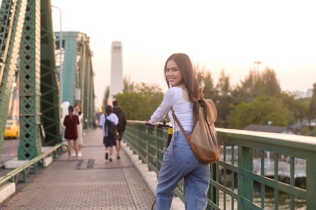 近代的な都市の背景に橋を渡る電動スクーターを持つ若い美しい女性の肖像画