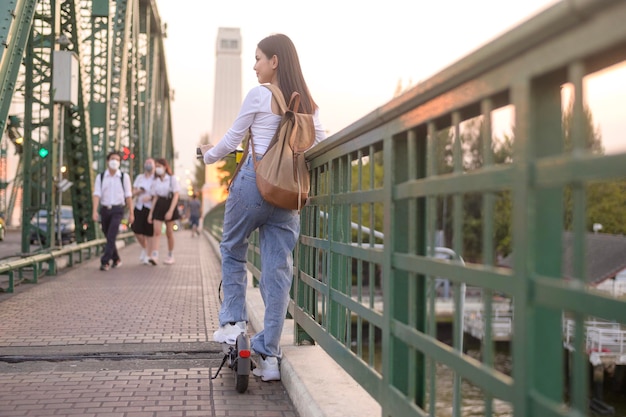 Portrait of young beautiful woman with an electric scooter over bridge in modern city background