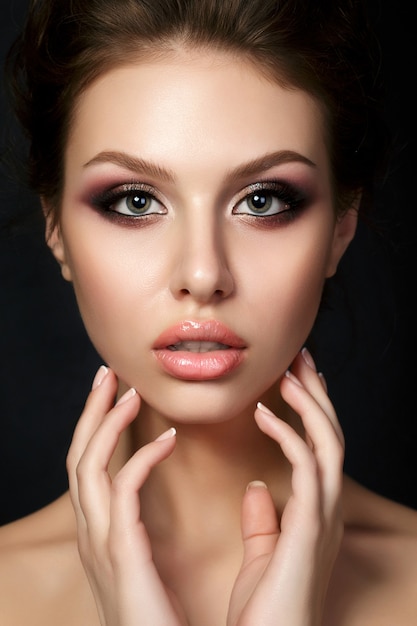 Portrait of young beautiful woman with evening make up touching her face over black background