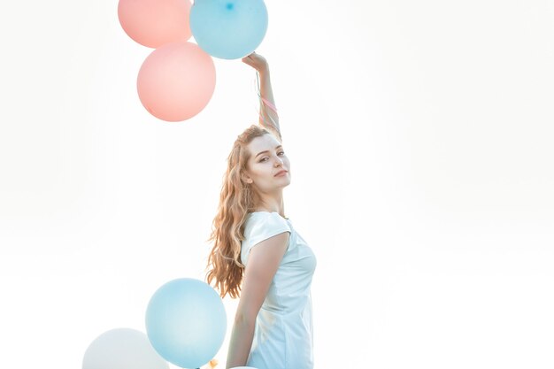 Portrait of young beautiful woman with flying multicolored balloons against the sky