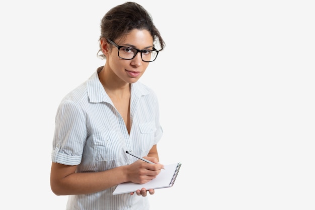 Portrait of a young beautiful woman with glasses writing with a pencil in a notebook