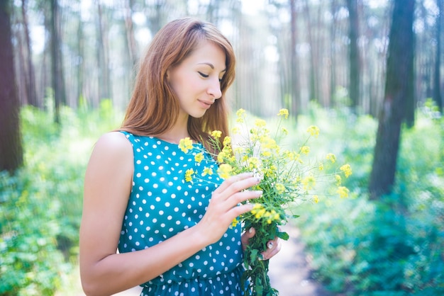 緑のぼやけた背景の上に黄色の花を保持している緑の目を持つ若い美しい女性の肖像画