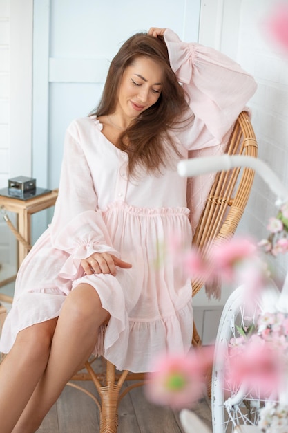 籐の椅子に座っているピンクのサマードレスを着ている長い髪の若い美しい女性の肖像画n