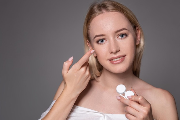 Portrait of young beautiful woman with natural makeup and contact eye lens in hand. Close-up of female model holding white lens box. Eye care and healthy lifestyle. Eyes health.