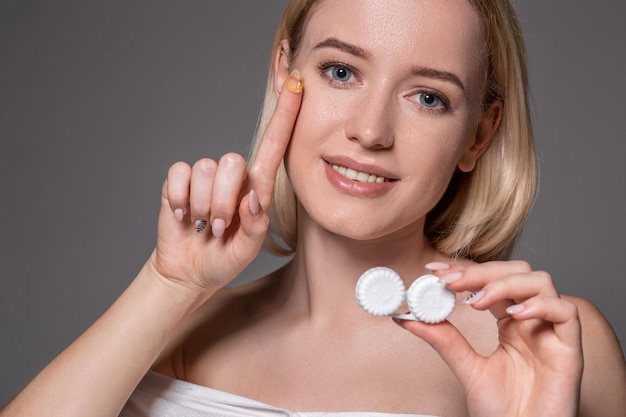 Portrait of young beautiful woman with natural makeup and contact eye lens in hand. Close-up of female model holding white lens box. Eye care and healthy lifestyle. Eyes health.