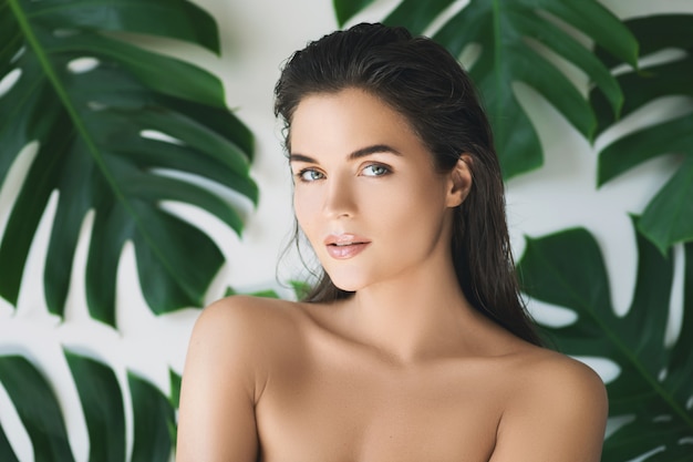 Photo portrait of young and beautiful woman with perfect smooth skin in tropical leaves