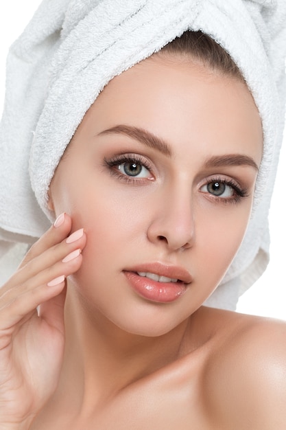 Portrait of young beautiful woman with towel on her hair touching her face isolated