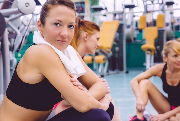 Portrait of young beautiful woman with towel resting sitting on the floor of fitness center after hard training day