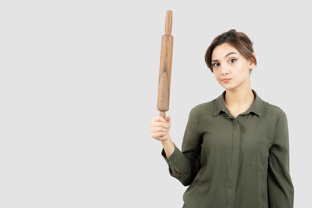 Portrait of young beautiful woman with wooden rolling pin standing. High quality photo