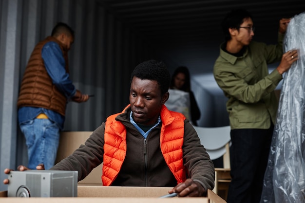 Portrait of young black man at outdoor auction opening\
cardboard boxes by storage container