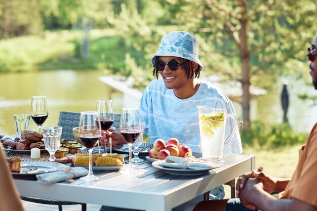 Portrait of young black man smiling at table while enjoying dinner party with friends outdoors in su