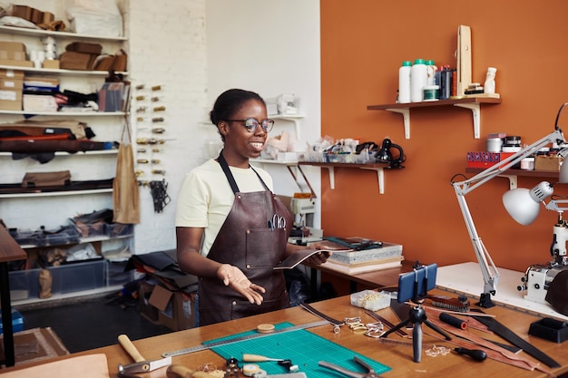 Portrait of young black woman in leatherworking shop recording video and promoting small business on