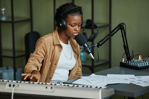 Portrait of young black woman singing to microphone while recording music at home