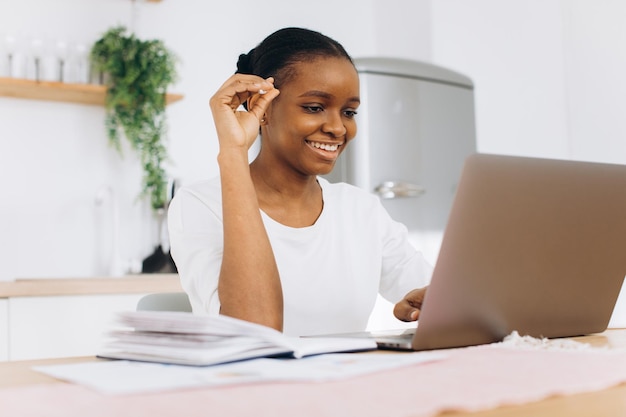 Portrait of a young black woman sitting in the kitchen and working on a laptop from home