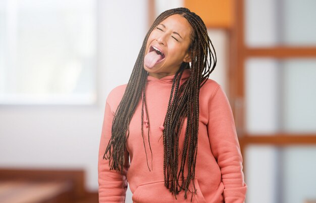 Portrait of a young black woman wearing braids expression of confidence and emotion, fun and friendly, showing tongue as a sign of play or fun