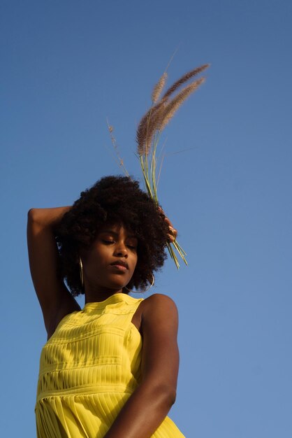 Portrait of a young black woman wearing yellow dress holding grass