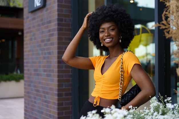 Ritratto di giovane donna nera con acconciatura afro sorridente in background urbano