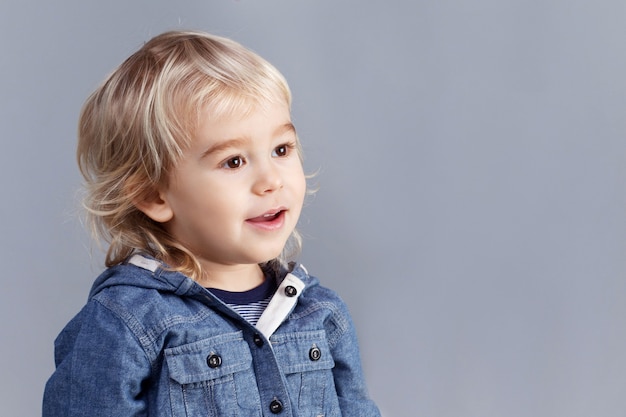 Portrait of a young blond boy on gray background. A three years boy looks into the distance